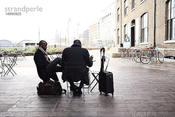 Zwei reisende Geschäftsleute sitzen im Straßencafé und arbeiten