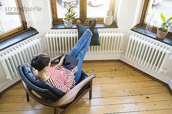 Kurzhaarige Frau entspannt sich in Lounge Chair mit Tablette in stilvoller Wohnung