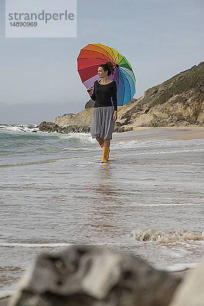 Frau mit buntem Regenschirm am Strand stehend