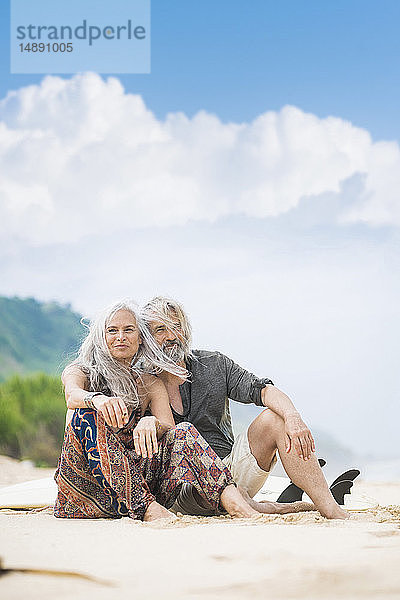 Porträt eines glücklichen älteren Hippie-Paares  das Seite an Seite am Strand sitzt