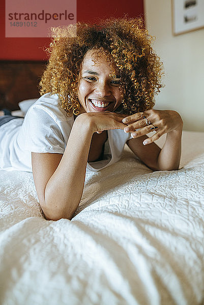 Porträt einer glücklichen jungen Frau mit lockigem Haar  die zu Hause auf dem Bett liegt