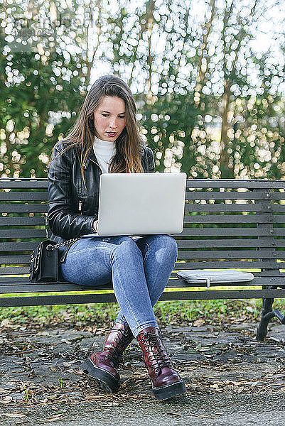 Junge Frau sitzt mit Laptop auf einer Parkbank