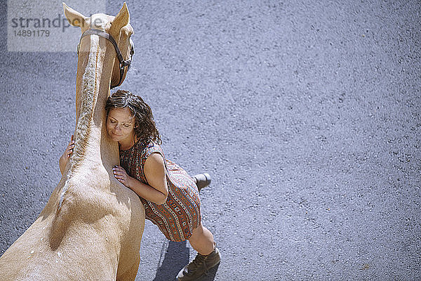 Überdachte Ansicht einer schwangeren Frau  die ein Pferd auf Tarnac im Sonnenlicht umarmt