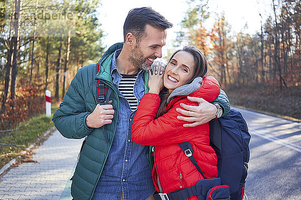 Glückliches Paar umarmt sich auf einer Straße im Wald während einer Rucksacktour