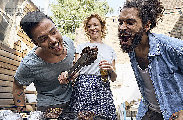 Freunde beim Grillen im Hinterhof  bei der Zubereitung von Fleisch auf dem Grill