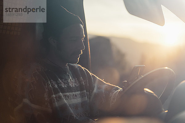 Junger Mann auf einer Autoreise mit einem Smartphone