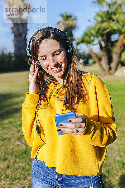 Glückliche junge Frau mit Handy  die mit Kopfhörern Musik hört