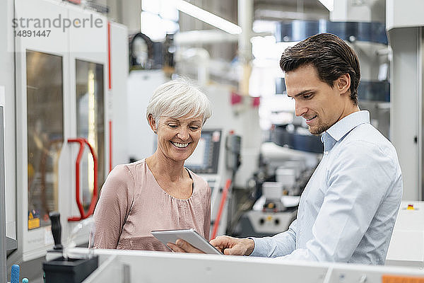 Lächelnder Geschäftsmann und ältere Frau mit Tablettengespräch in einer Fabrik