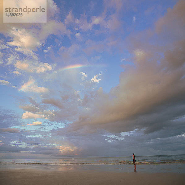 Wolkenlandschaft über einer am Strand spazierenden Frau in Port Douglas  Australien