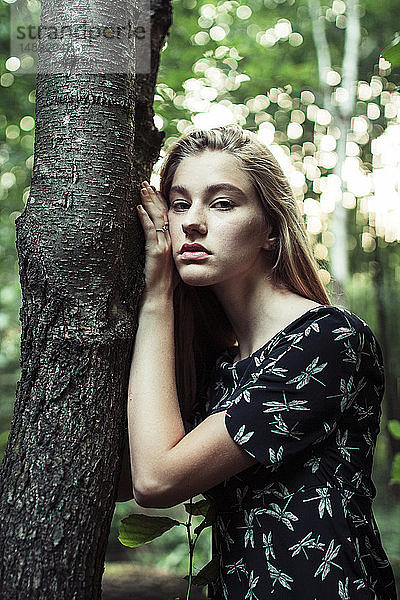 Junge Frau lehnt sich an einen Baumstamm