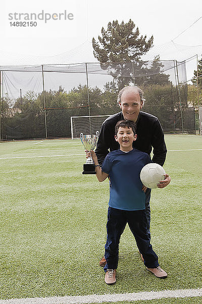 Vater mit seinem Sohn  der einen Fußball und eine Trophäe hält