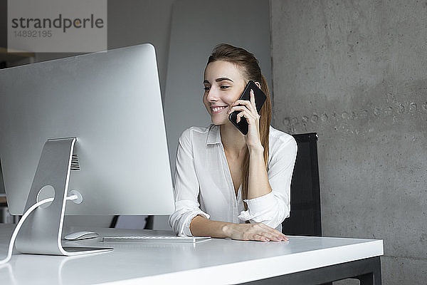 Lächelnde Geschäftsfrau  die ein Telefongespräch am Schreibtisch entgegennimmt