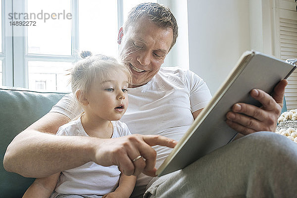 Vater liest seiner Tochter auf dem Sofa ein Buch vor