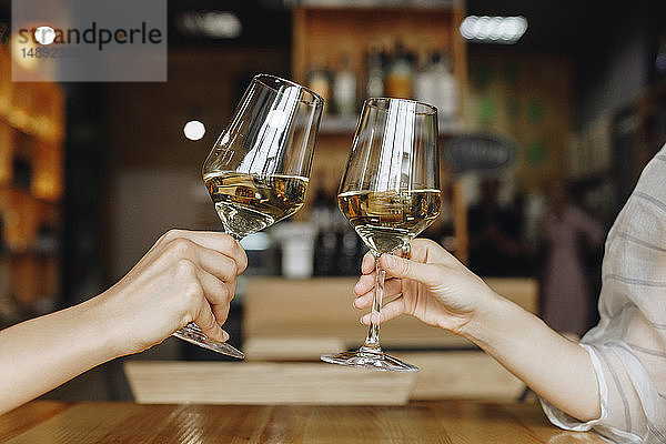Frauenhände  die mit einem Glas Weißwein anstoßen