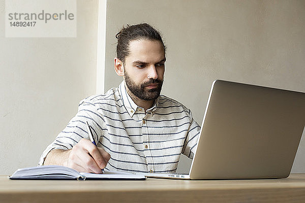 Junger Geschäftsmann mit Laptop schreibt in Notizblock