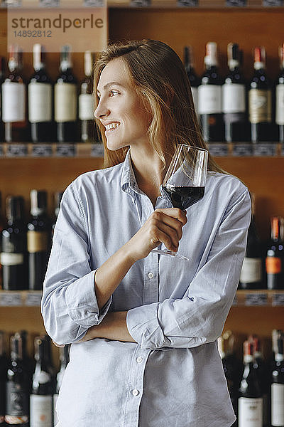 Lächelnde junge Frau hält ein Glas Rotwein