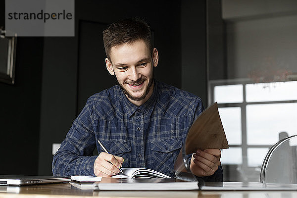 Lächelnder junger Geschäftsmann schreibt in einen Notizblock