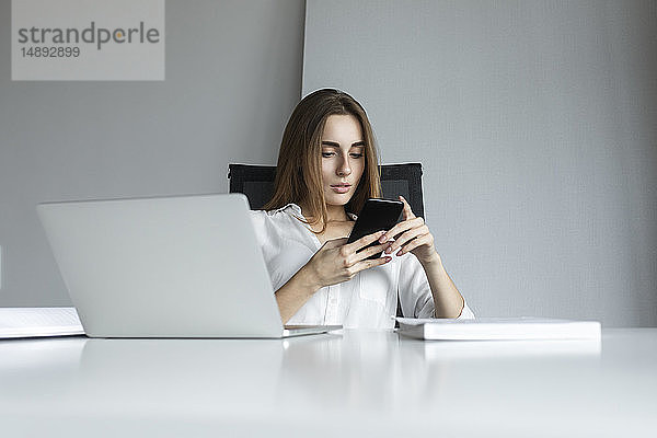 Junge Geschäftsfrau mit Textnachrichten am Schreibtisch