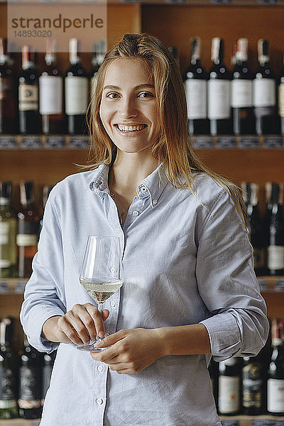Lächelnde junge Frau hält ein Glas Weißwein