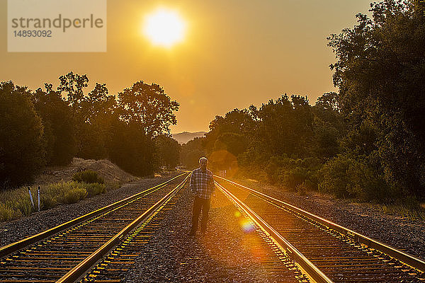 Älterer Mann steht bei Sonnenuntergang zwischen Eisenbahnschienen