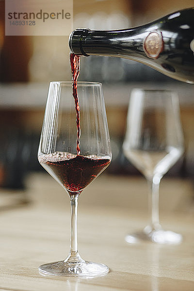Rotwein aus der Flasche in ein Weinglas gegossen