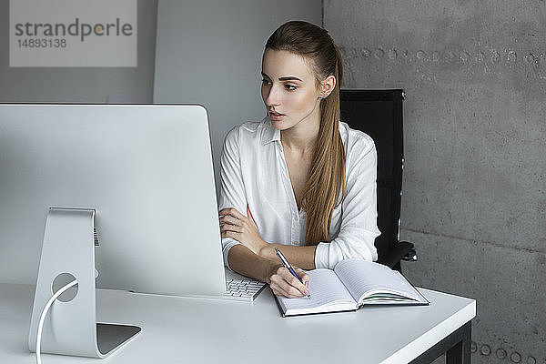 Junge Geschäftsfrau macht sich Notizen bei der Arbeit am Computer