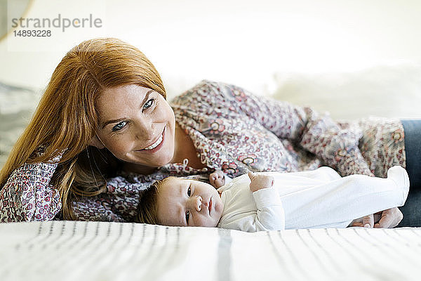 Lächelnde Frau mit ihrem neugeborenen Sohn auf einem Bett liegend