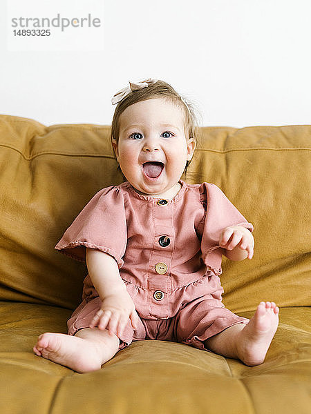 Baby Mädchen trägt rosa Outfit auf Sofa