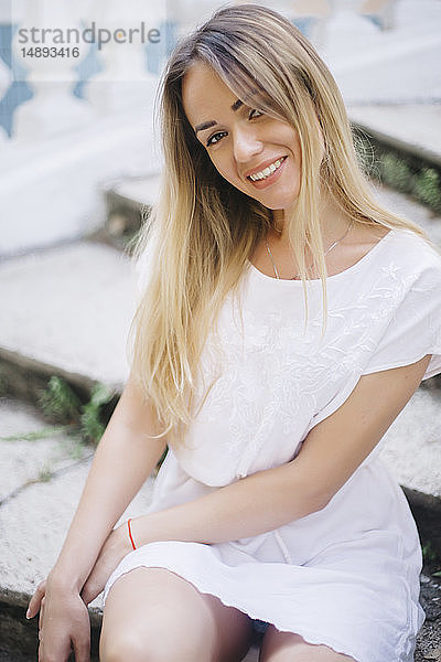 Junge Frau in weißem Kleid auf einer Treppe sitzend