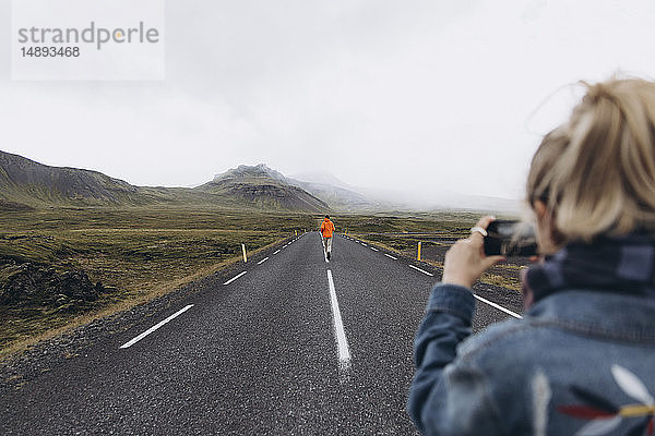 Junge Frau fotografiert ihren Freund beim Gehen auf der Landstraße in Island