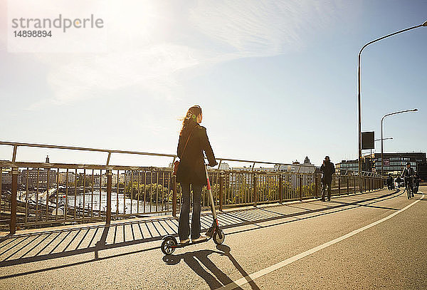 Frau in voller Länge auf Elektroschubroller auf Brücke gegen blauen Himmel