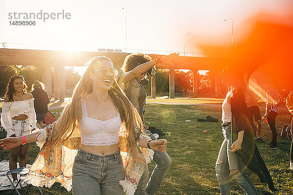 Fröhliche junge Frau tanzt mit Freunden an einem sonnigen Tag bei einer Musikveranstaltung