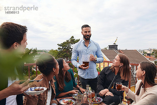 Mann unterhält sich mit Freunden bei einem Drink auf der Terrasse