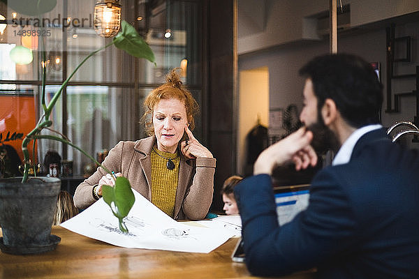 Selbstbewusste Grafikerinnen und Grafiker diskutieren bei Tisch im Büro über das Zeichnen auf Papier