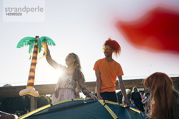 Frau hält Ballon  während sie mit Freunden am sonnigen Tag mit dem Zelt gegen den Himmel zeltet