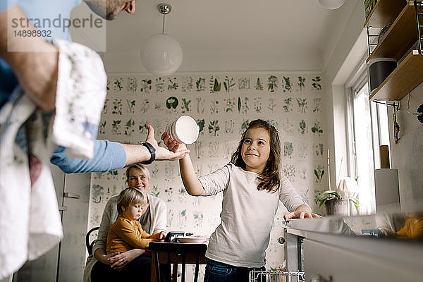 Lächelnde Tochter überreicht dem Vater zu Hause in der Küche eine Tasse