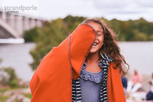 Fröhliches Mädchen mit orangefarbener Decke beim Picknick im Park