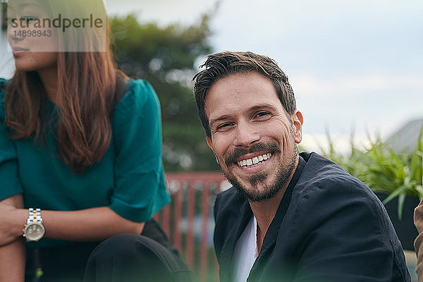 Porträt eines lächelnden bärtigen Mannes  der mit einem Freund auf der Terrasse feiert