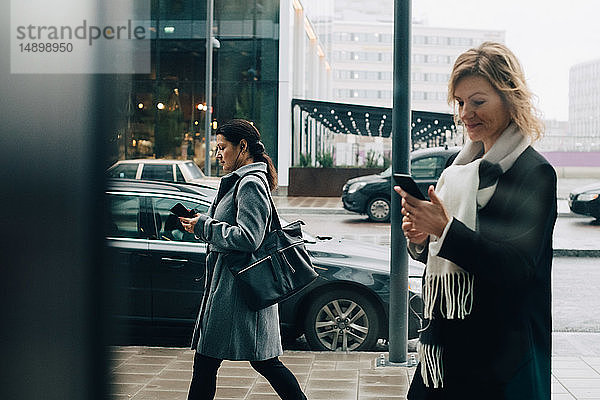 Geschäftsfrauen mit Smartphones beim Gehen auf dem Bürgersteig in der Stadt