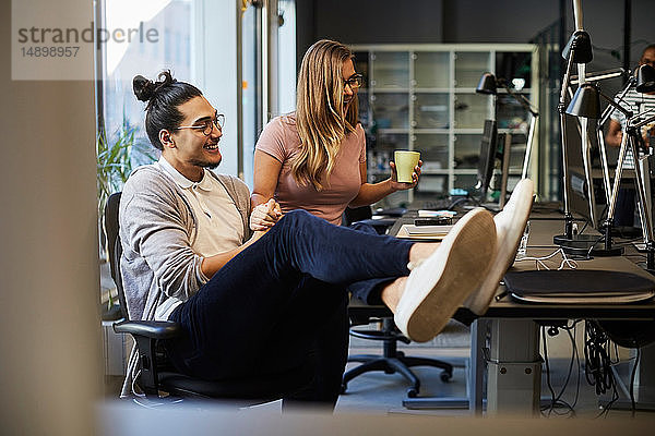 Lächelnde Unternehmer und Unternehmerinnen beim Blick auf den Laptop im Kreativbüro