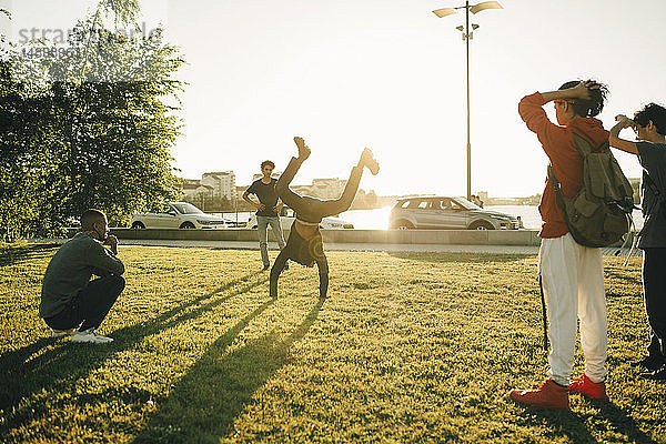 Freunde beobachten Teenager beim Handstand auf dem Feld an einem sonnigen Tag