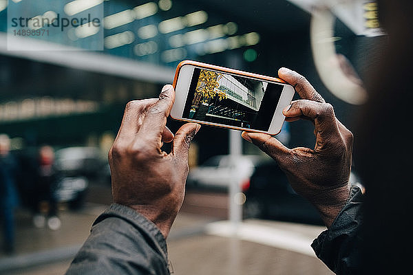 Abgetrennte Hände eines Geschäftsmannes  der in der Stadt ein Gebäude mit einem Smartphone fotografiert