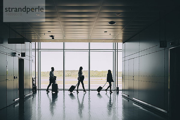 Seitenansicht der Silhouette von Geschäftskollegen  die beim Gehen im Korridor am Flughafen Gepäck ziehen