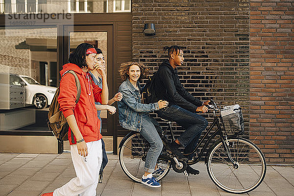 Fröhlicher junger Mann sieht Freunden beim Fahrradfahren in der Stadt zu