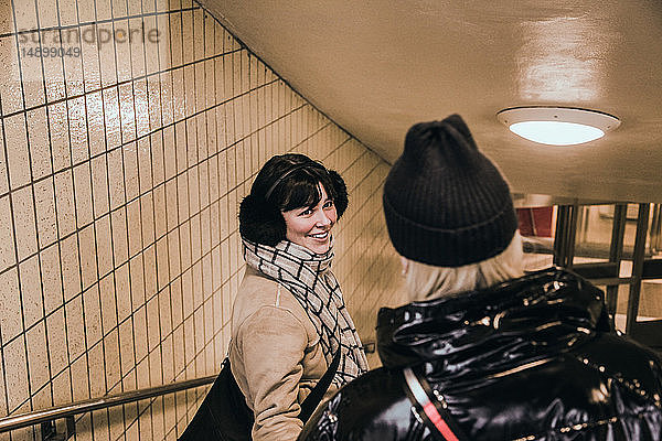 Lächelnde junge Frau in warmer Kleidung  während sie einen Freund in der U-Bahn anschaut