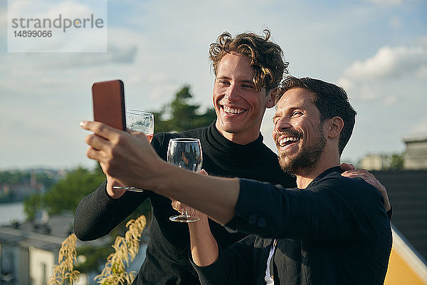 Fröhliche männliche Freunde beim Selfie mit Handy auf der Terrasse