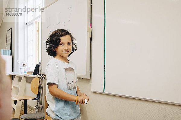 Lächelnder Junge steht an der Tafel im Klassenzimmer