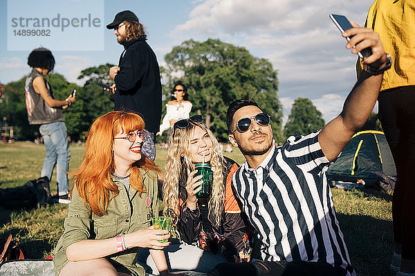 Junger Mann nimmt Selfie mit Freunden auf Smartphone während Musikkonzert im Sommer
