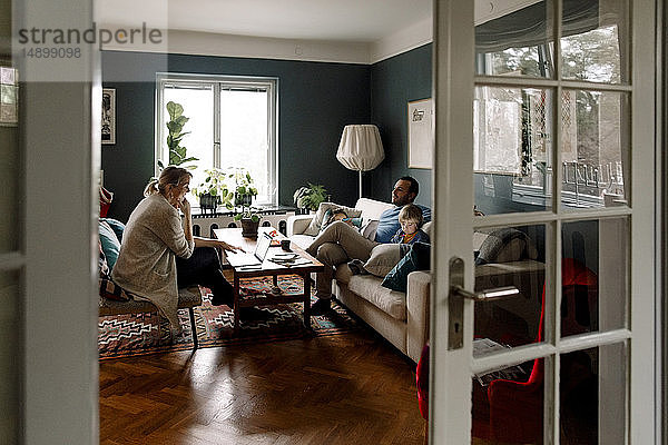 Familie  die verschiedene Technologien im Wohnzimmer benutzt  durch die Tür zu Hause gesehen
