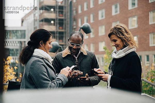 Kollegen  die Mobiltelefone benutzen  während sie in der Stadt gegen Gebäude stehen